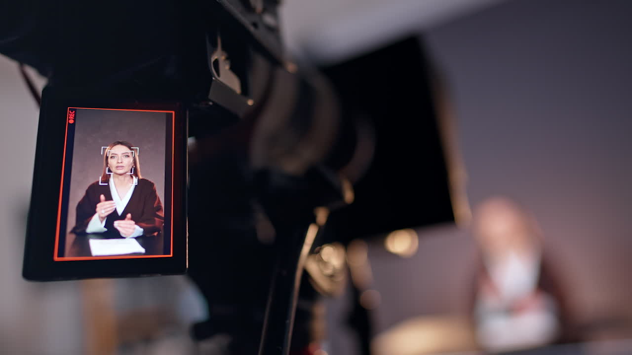 Display of camera showing a lady in brown outfit talking. Low angle view at the equipment recording a video for blog. Close up. Blurred backdrop.