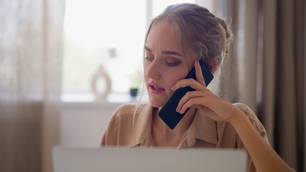 Young freelance woman talks on phone working on laptop