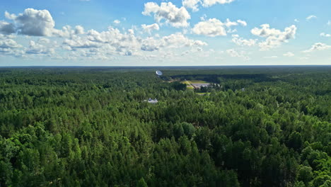 Radio-telescope-signal-booster-in-the-forest,-aerial-dense-spruce-tree-nature