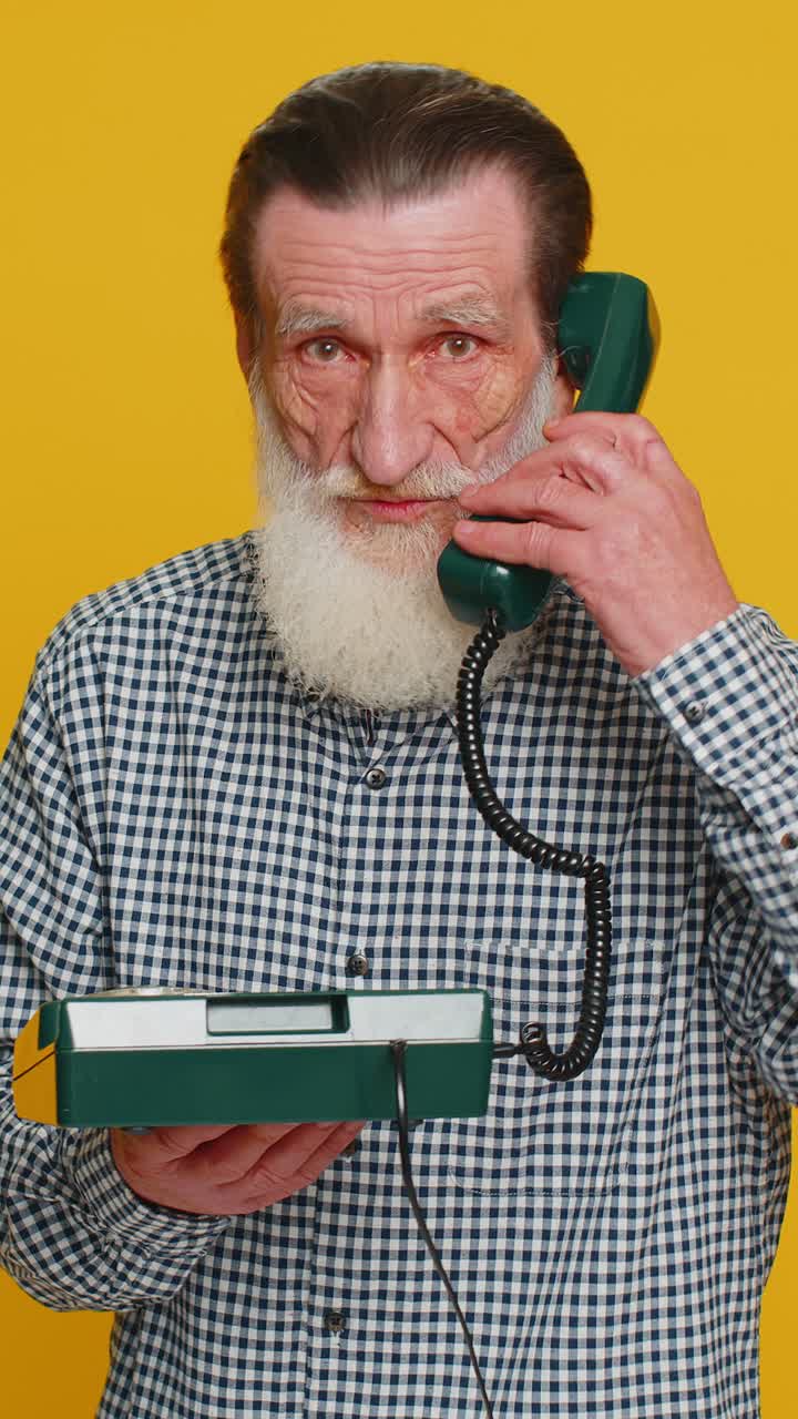Senior man talking on wired landline vintage telephone advertising proposition of conversation