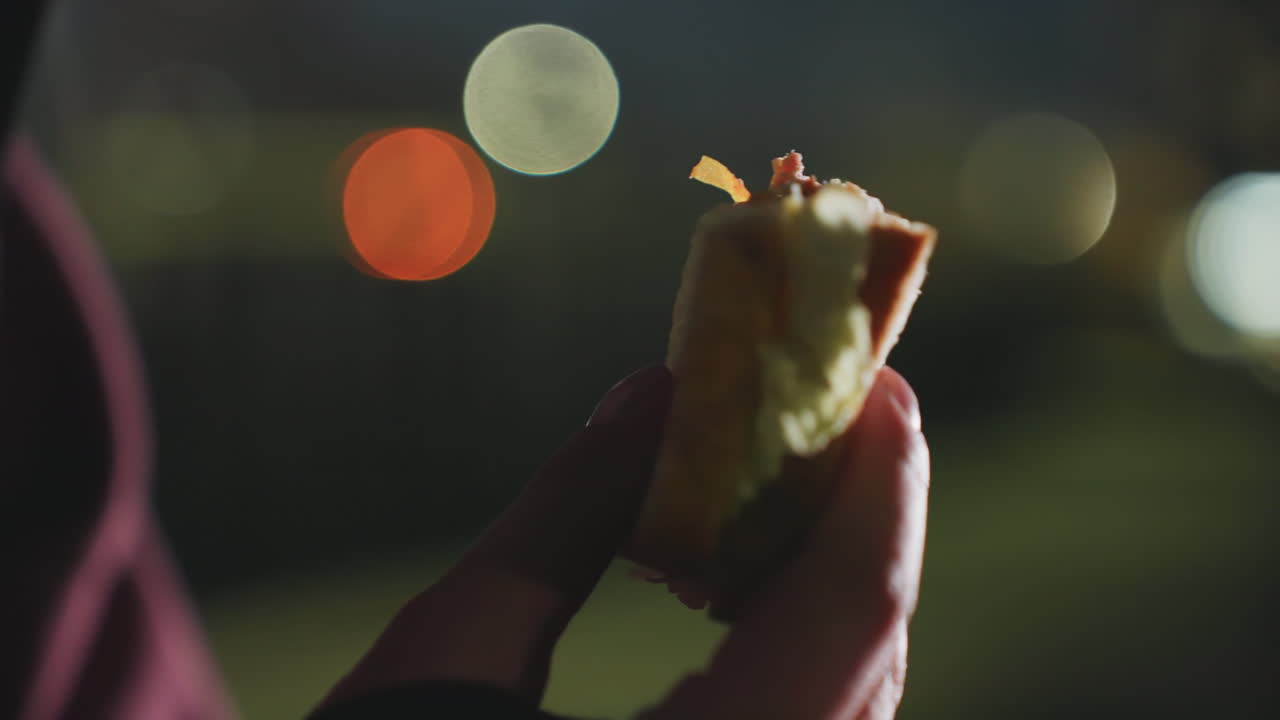 Close up hands of strength trainer holding torn bread outdoors on bench at twilight under blurred city lights for post workout nourishment and reflective recovery moment by dusk urban scene