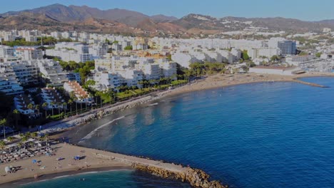 Drone-shot-with-pan-and-and-angled-forward-movement-filming-the-beach-at-Marbella,-Spain