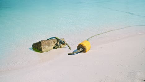 stone tied with thick rope used as anchor near yellow floating tool on sandy beach