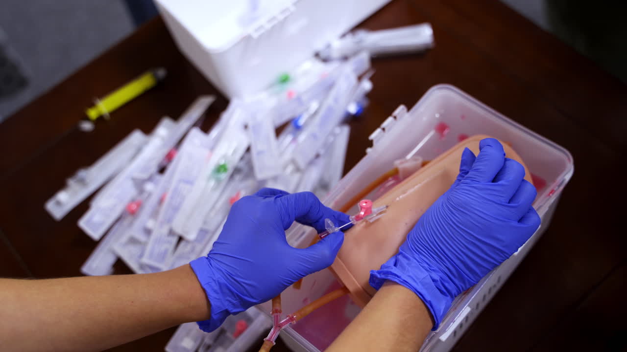Dummy for practicing inserting catheter. Hands in blue latex gloves with medical neddle. Selective focus from above.