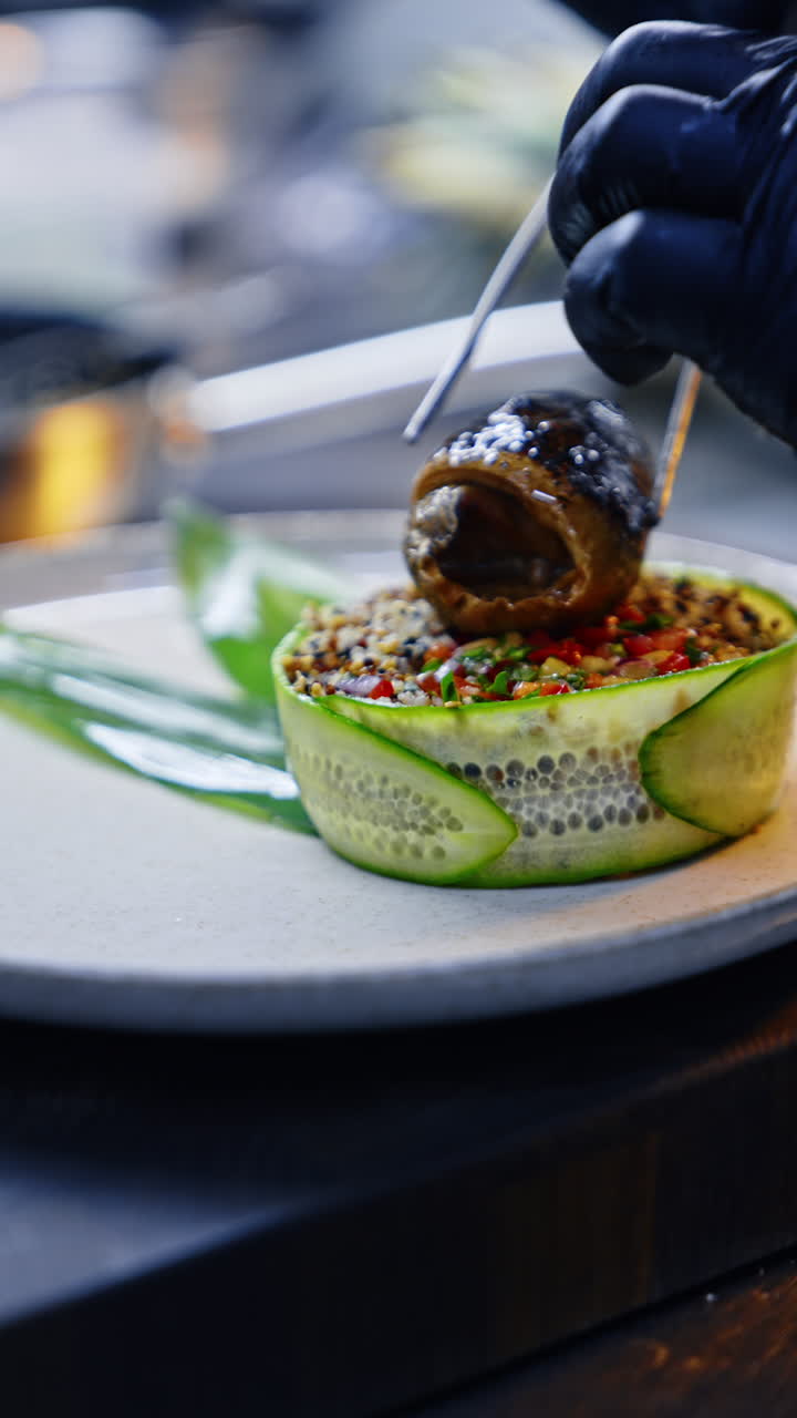 Fried fish roll is placed on the vegetable. Unrecognized cook in black gloves serves the fish dish. Close up. Vertical video.