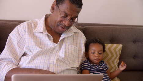 Großvater-Und-Enkel-Sitzen-Zu-Hause-Mit-Laptop-Auf-Dem-Sofa