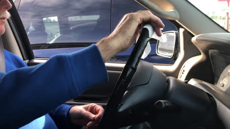 person using disinfecting wipes to clean steering wheel of the car - close up, side view