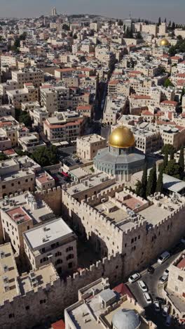 aerial view of a golden domed shrine nestled within ancient fortified walls, surrounded by a sprawling cityscape of modern and traditional buildings, highlighting the blend of history and modernity