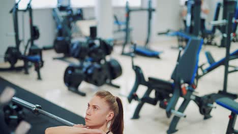 Young woman with a tail performs squats with a barbell in the gym on the background of the interior of a fitness club. Blurred Background