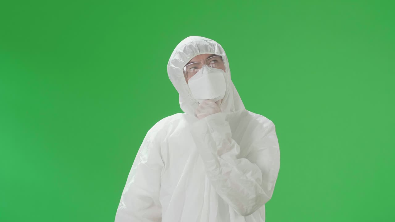 Asian Man Wearing Personal Protective Equipment Uniform Ppe, Medical Face Mask And Thinking About Something And Looking Around Then Raising His Index Finger In The Green Screen Studio
