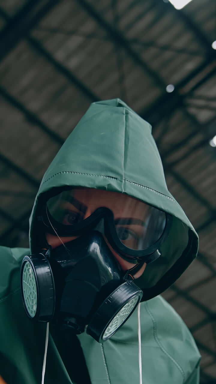 Portrait of a woman in safety suit and gas mask. Human wearing antibacterial costume trying to touch something with hand in glove in abandoned place. Gas attack. Vertical video