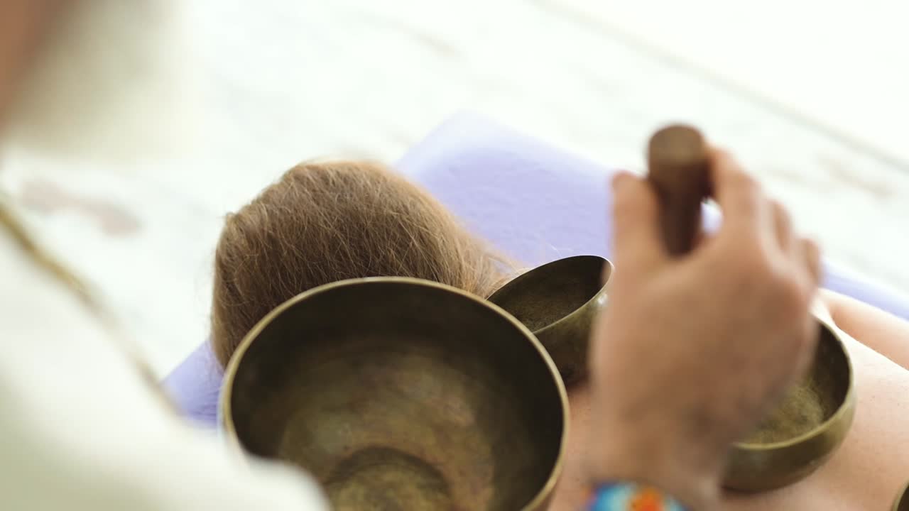 Crop sound therapist playing bowl gongs on back of woman