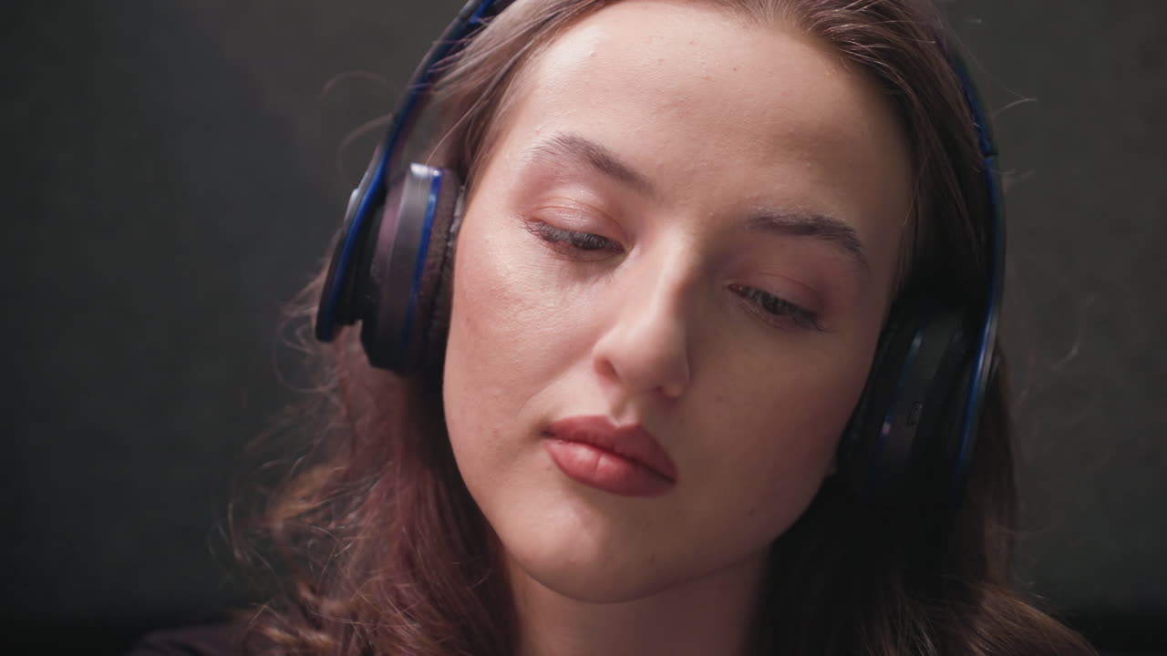 Close up of woman with soft lashes and brown hair wearing headset while calmly listening. Focused facial expression and subtle lighting highlight relaxed concentration and immersive moment