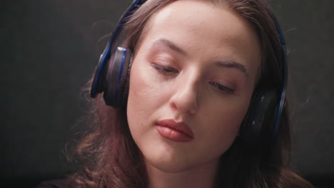 close up of woman with soft lashes and brown hair wearing headset while calmly listening. focused facial expression and subtle lighting highlight relaxed concentration and immersive moment