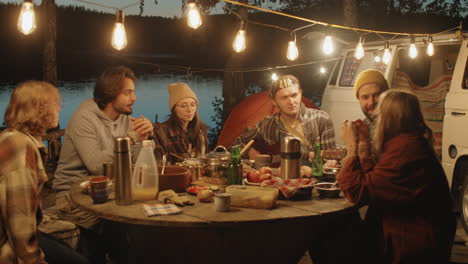 friends having dinner and playing guitar at campsite