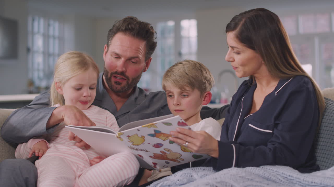 Famiglia sorridente seduta sul divano che legge insieme una favola della buonanotte da un libro.