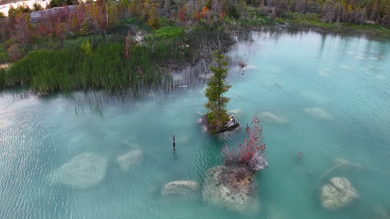 Aerial drone footage of a turquoise quarry lake with rocky formations and surrounding autumn foliage