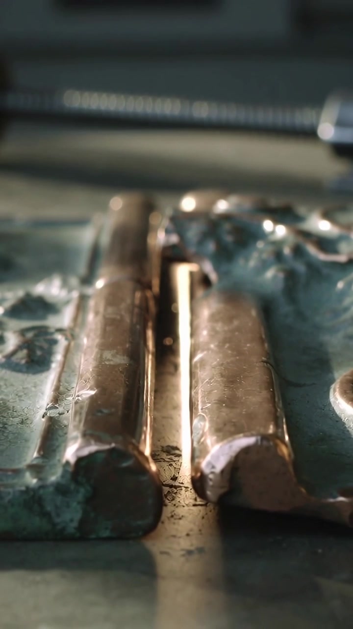 Video verticale: La messa a fuoco della telecamera si sposta rivelando un paio di barre di cerniera in bronzo su un banco da lavoro, con detriti.