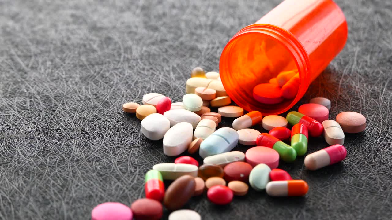 pastillas y cápsulas variadas esparcidas de un recipiente naranja