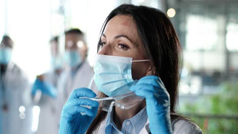 close up of pretty female physician taking off medical mask and safety glasses and looking at camera