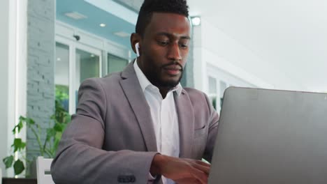 african american businessman using wireless earphones and laptop in cafe