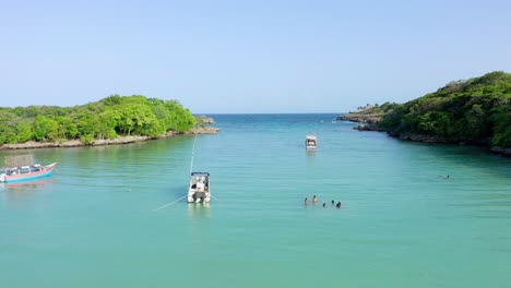 Aufnahme-Mit-Einer-Drohne,-Die-Die-Badegäste-Und-Drei-Boote-An-Einem-Klaren-Tag-Mit-Kristallklarem-Wasser-Am-Strand-Beobachtet,-Diamante-Cabrera,-Dominikanische-Republik