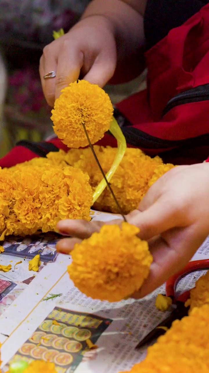 Primo piano di mani che infilano fiori di calendula gialli su un ago al mercato dei fiori di Bangkok
