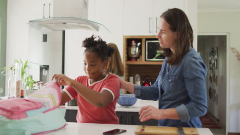 feliz mujer caucásica y su hija afroamericana empacando comida juntos