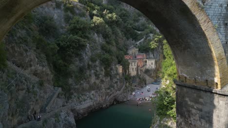 un dron cinematográfico filmado bajo un puente revela el fiordo di furore en la costa de amalfi, italia.