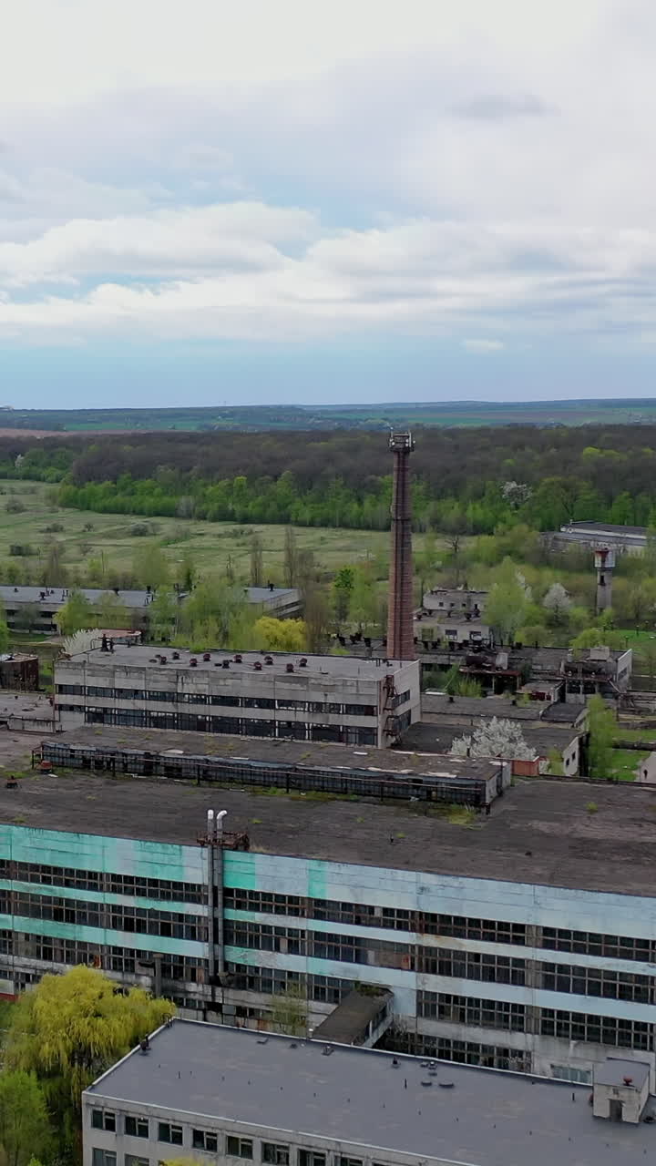 Large factory among beautiful green nature. Exterior of industrial plant in the countryside. Old architectural buildings of a manufacturing. Vertical video