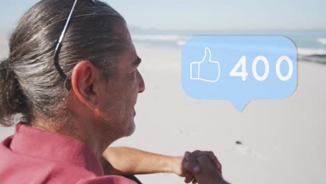 Animation-of-speech-bubble-with-thumbs-up-icon-and-numbers-over-senior-man-on-beach