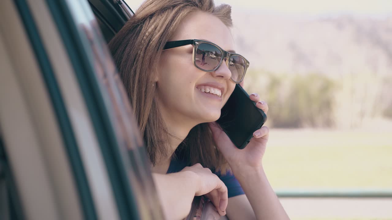 mujer sonriente con teléfono mira por la ventana abierta del automóvil