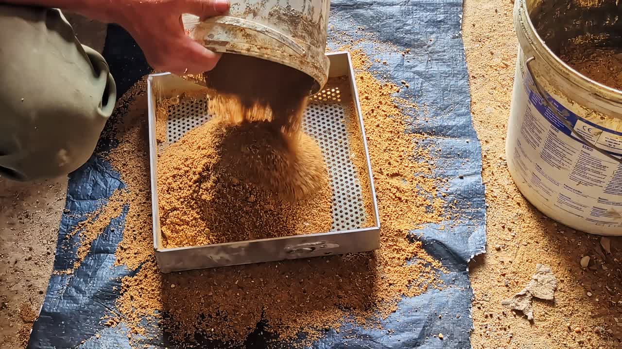 Worker sifting sand through metal sieve for masonry preparation on construction site
