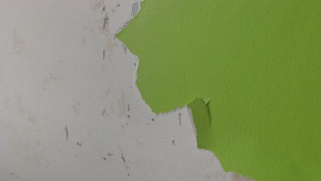 steady shot of a man scraping off green paint from a wall busy with renovations