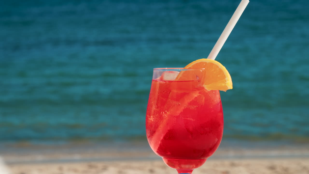 Un cocktail rinfrescante rosso-arancio con ghiaccio e fetta d'arancia sullo sfondo del blu intenso del Mar Mediterraneo