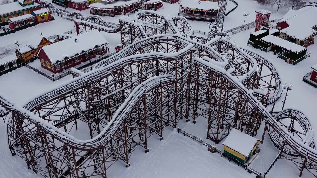Snow-covered roller coaster gracefully winds through an amusement park, highlighting the thrilling curves and architectural beauty of the ride in a serene winter landscape