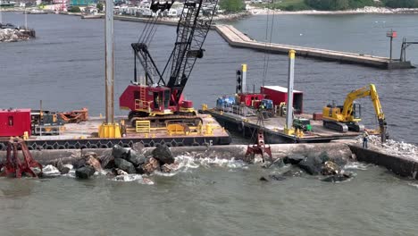 Using-a-grapple,-a-crane-moves-pieces-of-riprap-to-build-up-a-pier-in-Algoma,-WI-on-Lake-Michigan