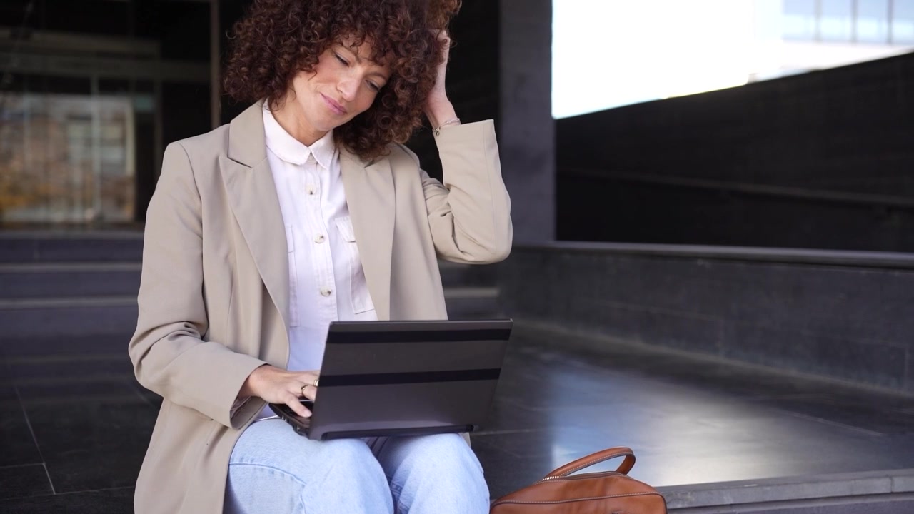 Una donna d'affari concentrata lavora al suo laptop all'aperto in un ambiente urbano frenetico.