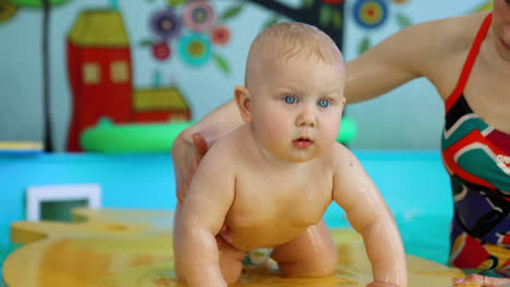 lovely caucasian baby boy stands on all four on the floating mat. little child in the swimming pool.