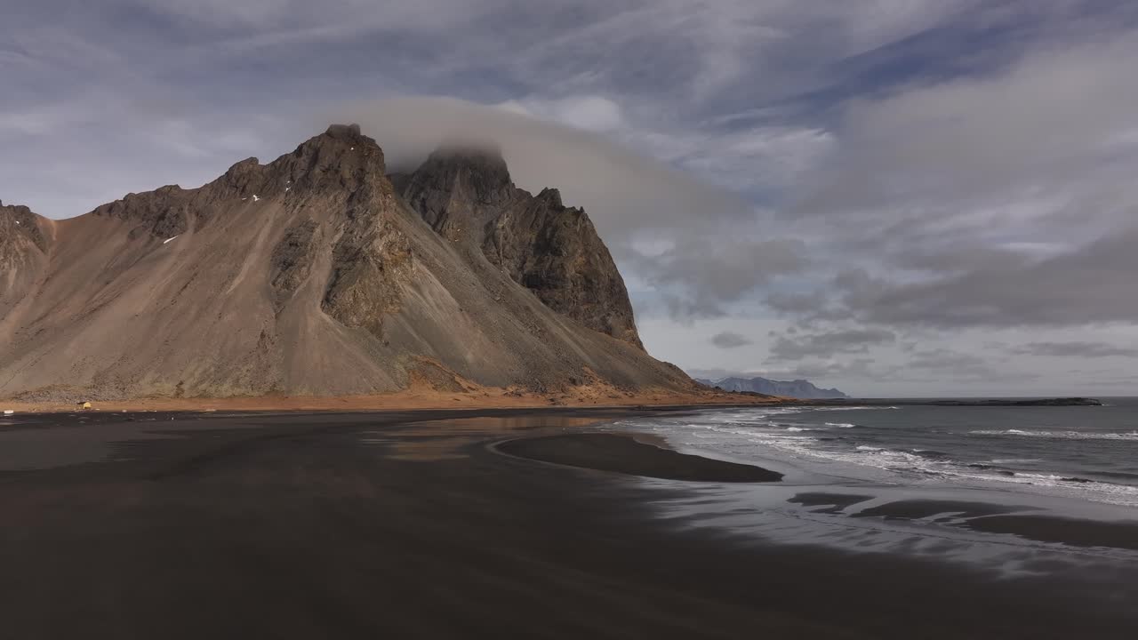 clouds hover above rugged peaks and dark shoreline near Stokksnes Iceland