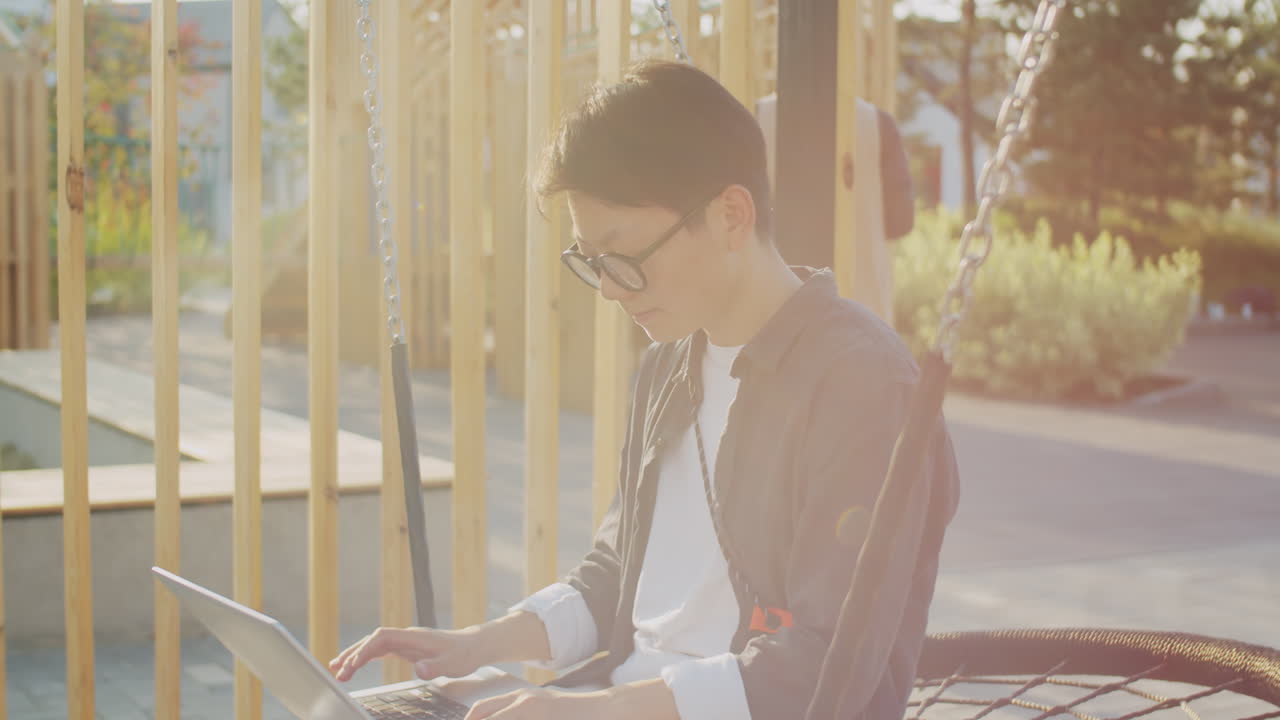 아시안 여성 프리랜서가 야외에서 스 ⁇ 에 앉아 노트북을 사용하고 있습니다.