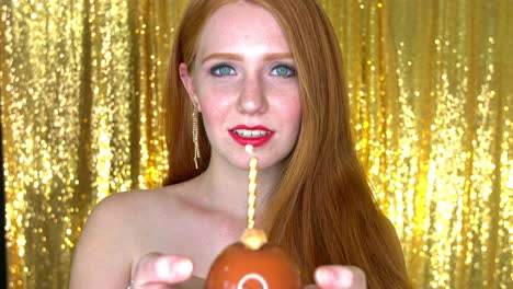 a beautiful young woman all dressed up,standing against golden shimmery background and holding a golden candle