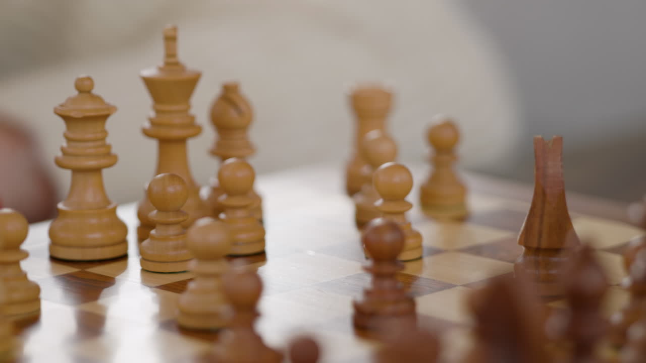 Una persona è concentrata su una partita a scacchi e sta muovendo un cavallo sulla scacchiera, mentre si vedono altri pezzi di legno. L'ambientazione è interna, con uno sfondo delicato.