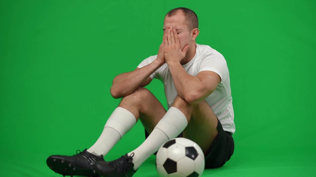 절망에 빠진 백인 축구 선수가 초록색 스크린에 축구 공을 들고 앉아서 손에 머리를 들고 한숨을 쉬고, 크로마케이 배경의 슬픈 불만족한 스포츠맨의 광장 촬영 초상화.