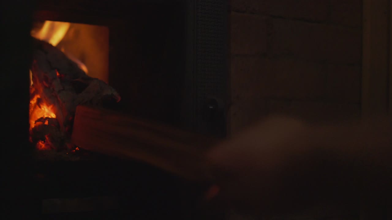 남자 손으로 유리 벽난로 문을 열고 나무 로그 내부를 추가합니다.