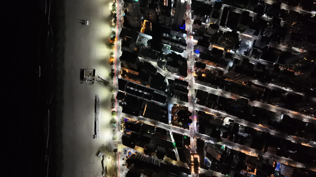 View of the Brazilian seaside city of Balneário Camboriú, with its skyscrapers all lit up at night and a sandy beach