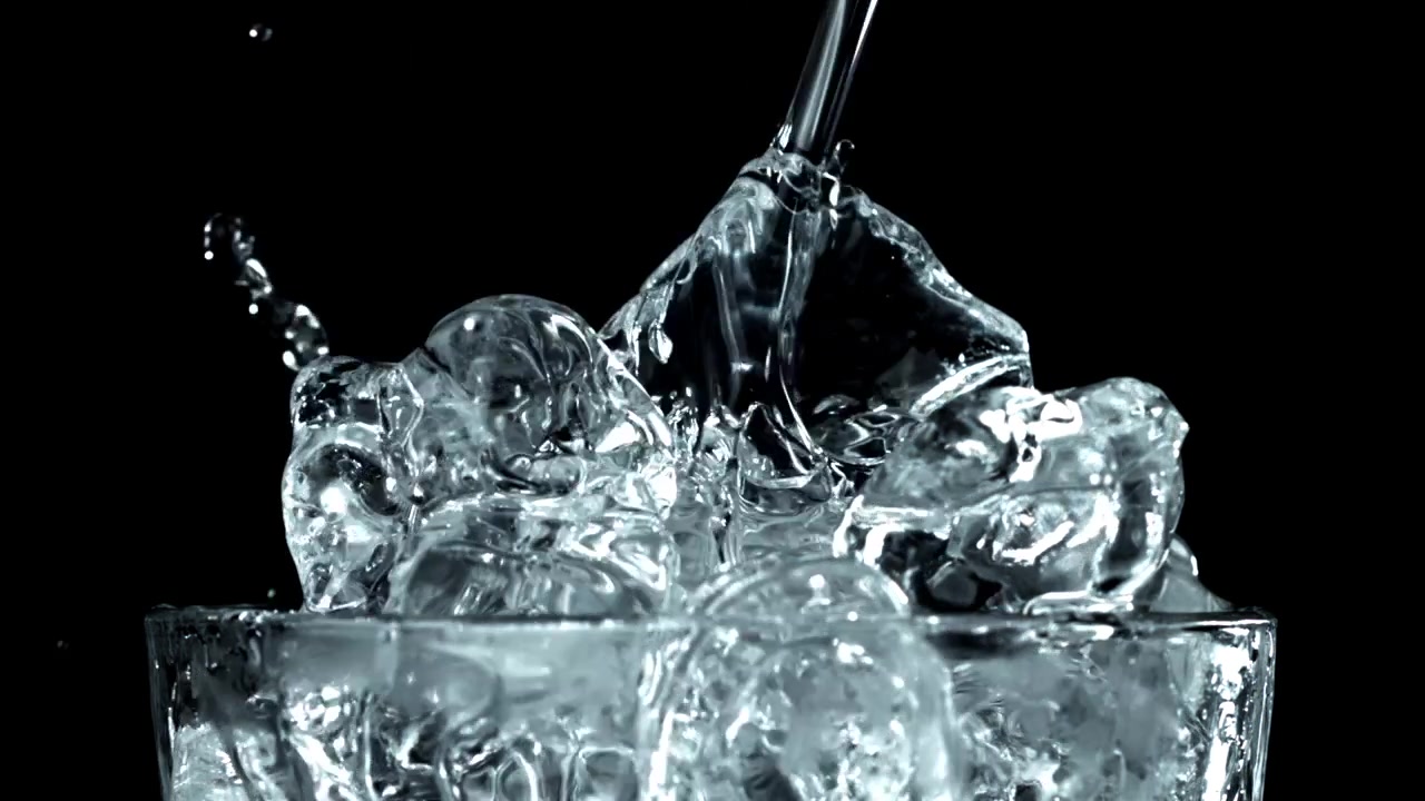 Acqua versata al rallentatore in un bicchiere con cubetti di ghiaccio