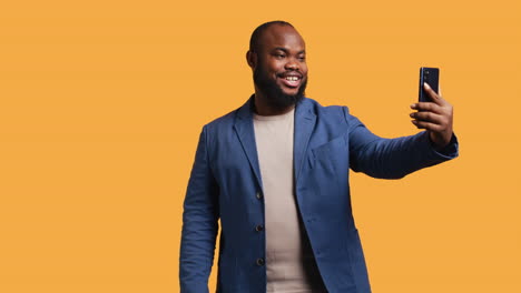 Joyous-man-using-smartphone-to-take-selfies,-studio-background