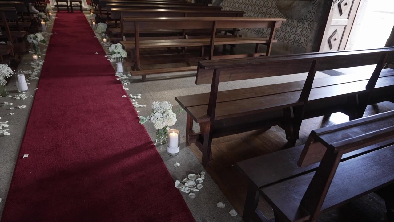Red carpet aisle with wooden pews, white flowers, and scattered petals in a church setting