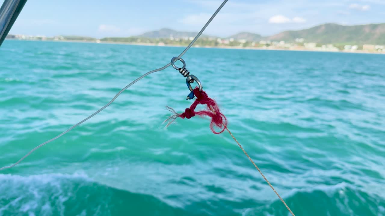 A fishing lure dances over turquoise ocean waves near Phuket, Thailand, under bright daylight, showcasing dynamic movement and vibrant colors